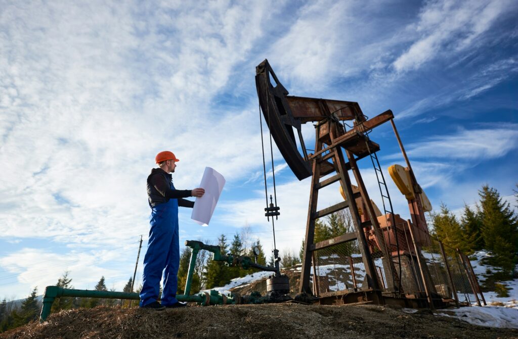 Oil worker standing in the oilfield next to a pump jack with a big paper